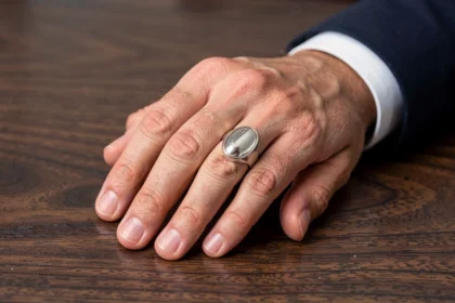 Chevalière homme personnalisée avec plateau ovale en argent massif portée sur la main droite, vue macro sur fond bois noyer